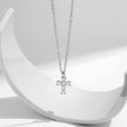 Silver cross pendant with six clear moissanite stones suspended over a curved white prop