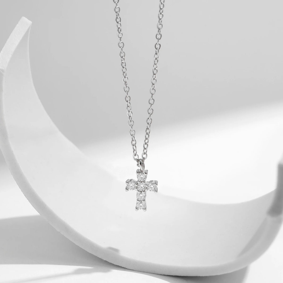 Silver cross pendant with six clear moissanite stones suspended over a curved white prop