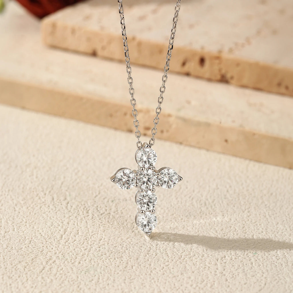 Close-up of the six round moissanite stone cross pendant on an elongated-link chain over a textured surface
