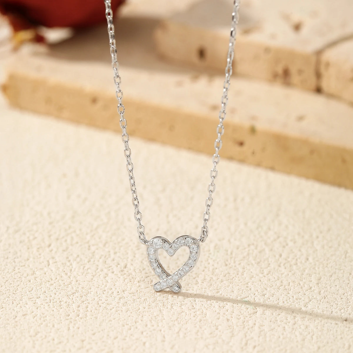 Close-up of the sterling silver moissanite ribbon heart pendant suspended over a textured surface
