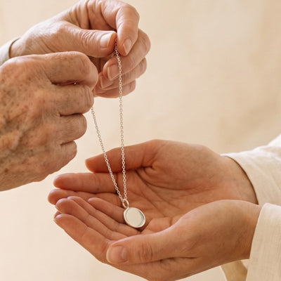 An older woman's hands passing a sterling silver necklace into a younger woman's hands