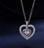 Close-up of the 925 sterling silver nested heart pendant with a moissanite center on a dark blue surface