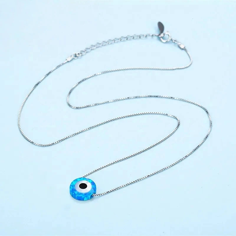 Blue synthetic opal evil eye necklace laid out with its adjustable chain and clasp on a pale blue background