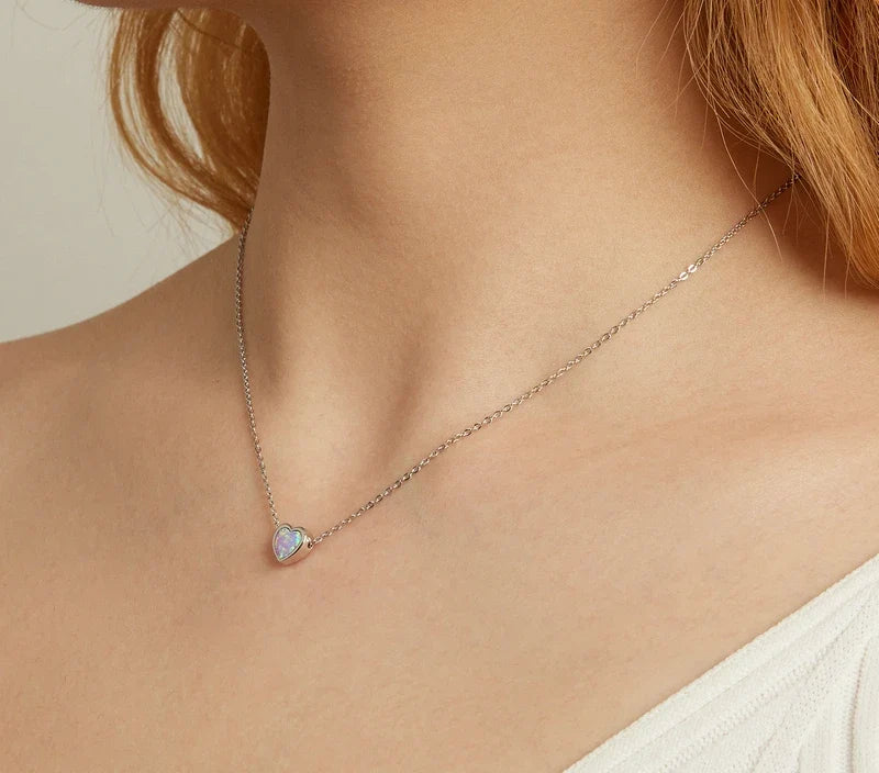 Small opal-look heart necklace worn at the collarbone with a polished silver-colored rim and fine chain