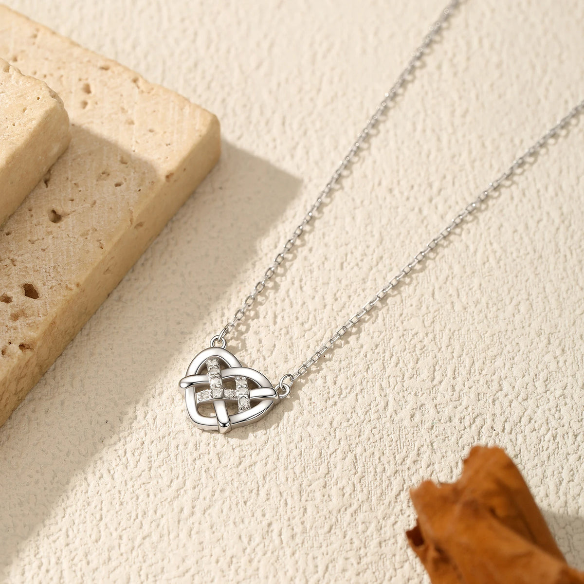 Close flat lay of the openwork heart pendant and elongated-link chain on a textured cream surface