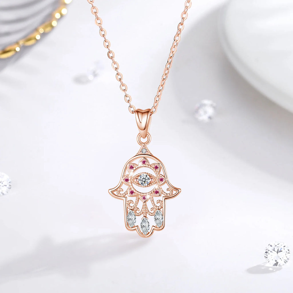 Rose gold-colored hamsa hand pendant with pink CZ stones and clear marquise stones displayed on a white surface