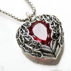 Close-up of the red CZ heart framed by antiqued feather details and small dark stones