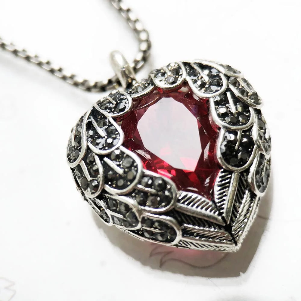 Close-up of the red CZ heart framed by antiqued feather details and small dark stones
