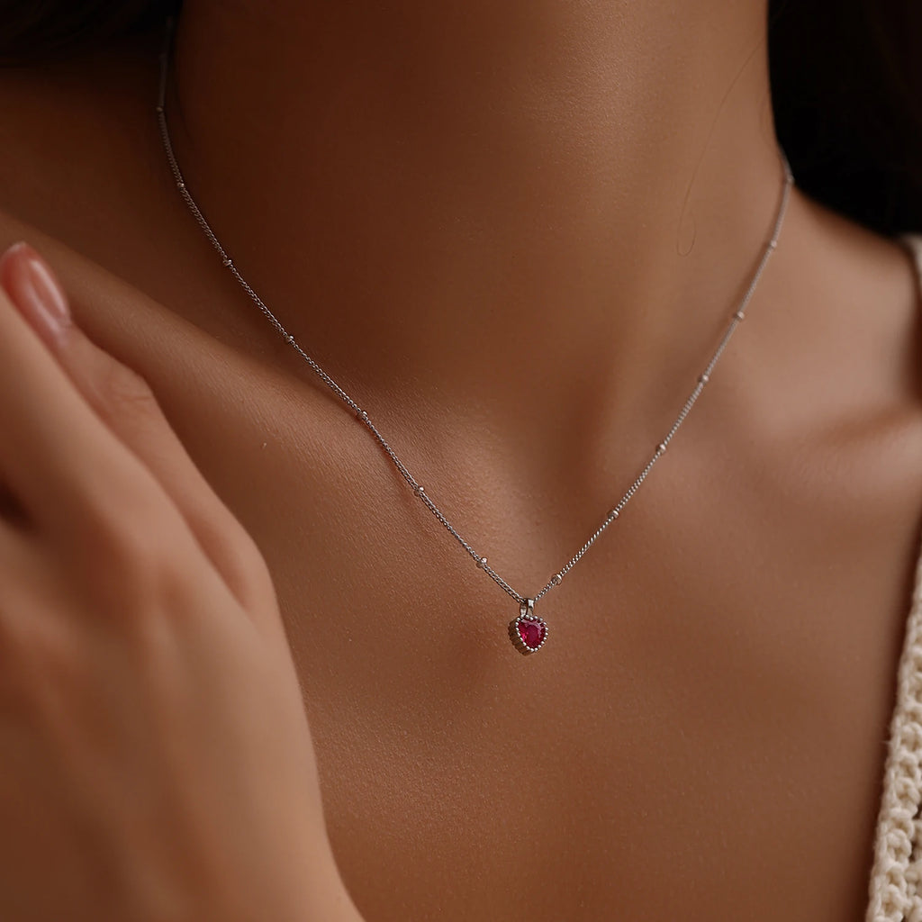 Small red heart pendant necklace worn at the base of the neck on a fine silver-tone chain