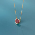 Dark red heart pendant with a gold-colored rim suspended from a fine chain on a blue surface