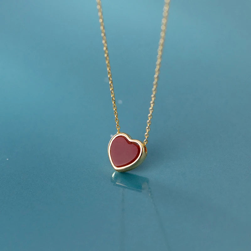 Dark red heart pendant with a gold-colored rim suspended from a fine chain on a blue surface