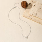 Sterling silver ribbon heart necklace arranged beside a dried flower and pale stone blocks