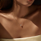 Sterling silver ribbon heart necklace with moissanite worn at the collarbone in warm side light