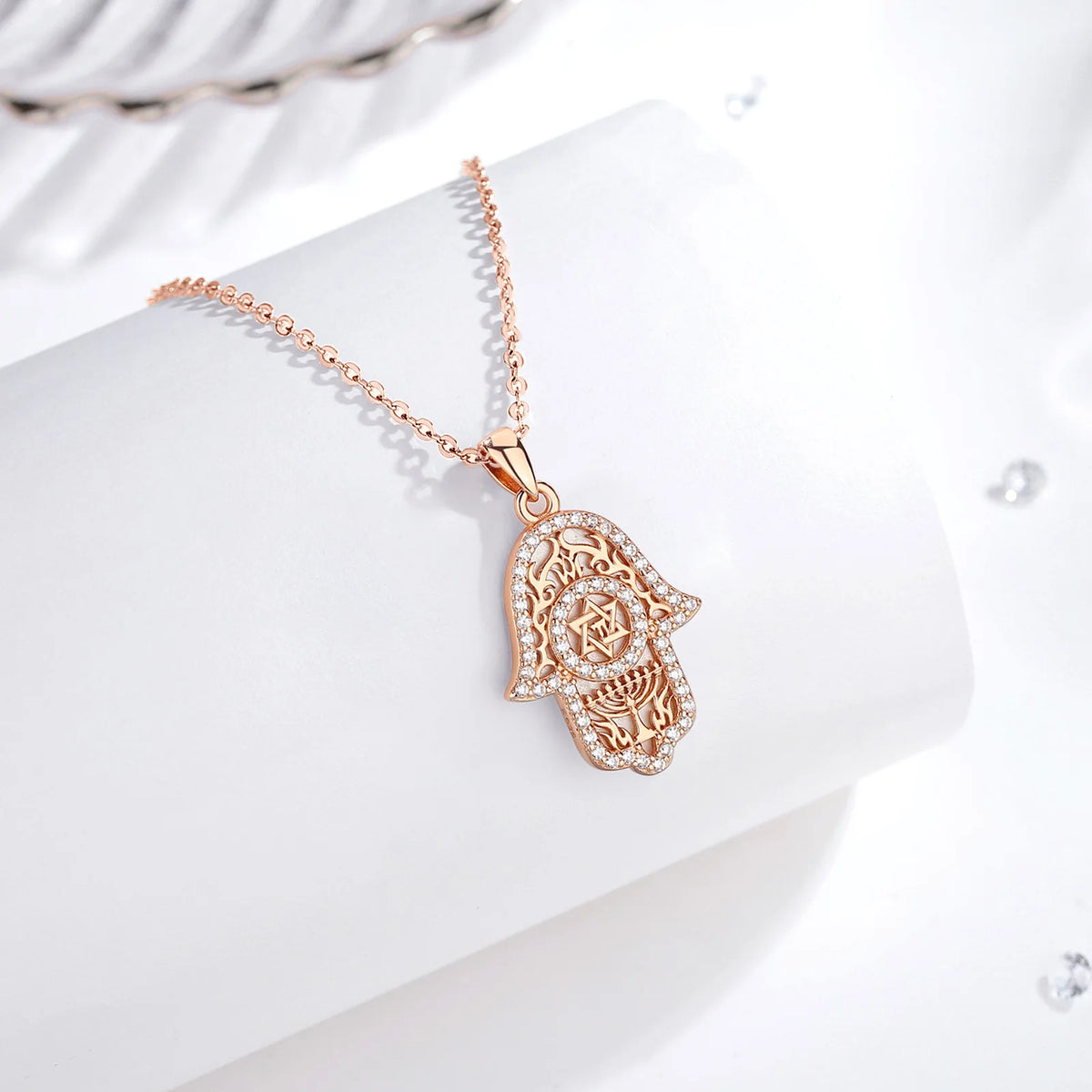 Rose gold Hamsa necklace arranged on a white curved display with Star of David and CZ stones