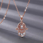 Close-up of the rose gold-colored hamsa pendant with open scrollwork, pink CZ stones and three clear hanging stones