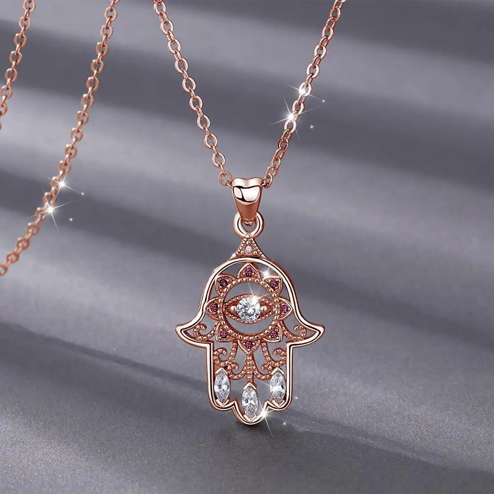 Close-up of the rose gold-colored hamsa pendant with open scrollwork, pink CZ stones and three clear hanging stones