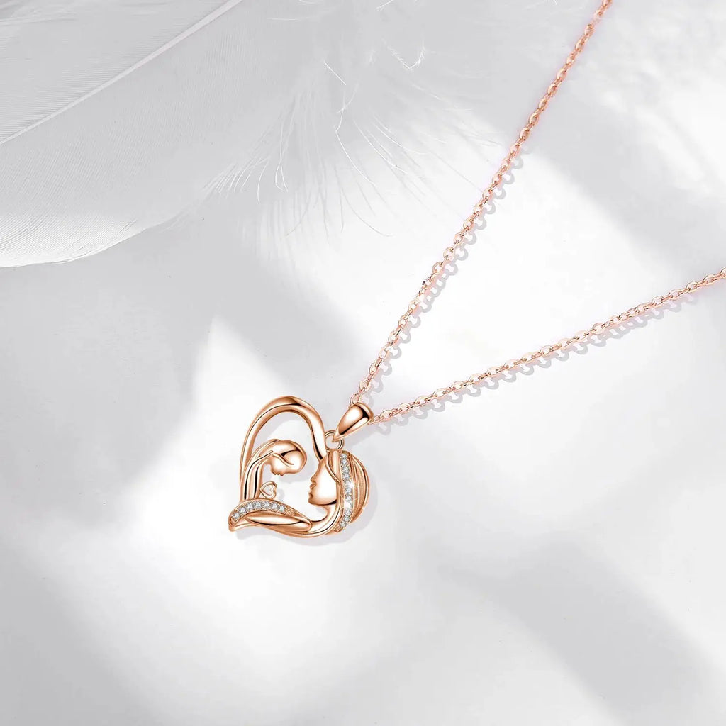 Rose gold-tone mother and child heart necklace arranged on a white surface with a feather