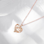 Rose gold-tone mother and child heart necklace arranged on a white surface with a feather