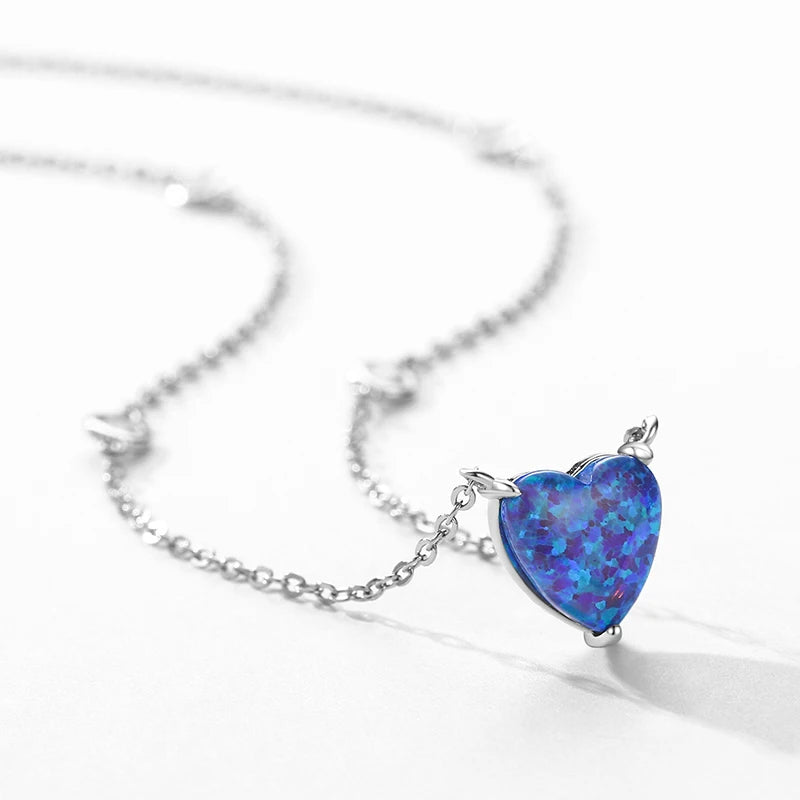 Close-up of a silver-tone heart pendant with a shifting blue opal-look stone and three prongs