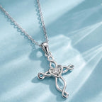 Silver-tone Celtic cross necklace on pale blue fabric with polished loops and a clear center stone