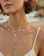 Silver-tone Celtic cross necklace worn at the collarbone with interlaced arms and heart center