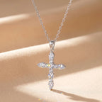 Silver-tone moissanite cross pendant with a flared bail displayed against a warm fabric background