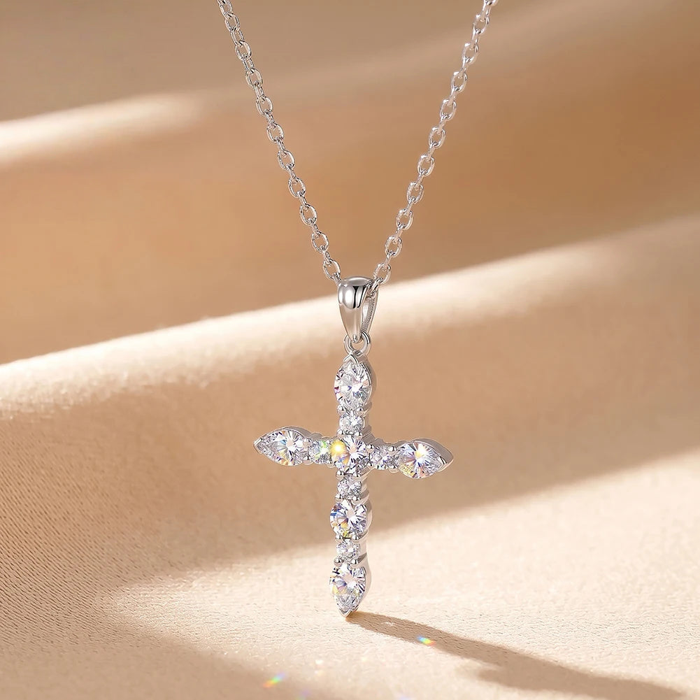 Silver-tone moissanite cross pendant with a flared bail displayed against a warm fabric background