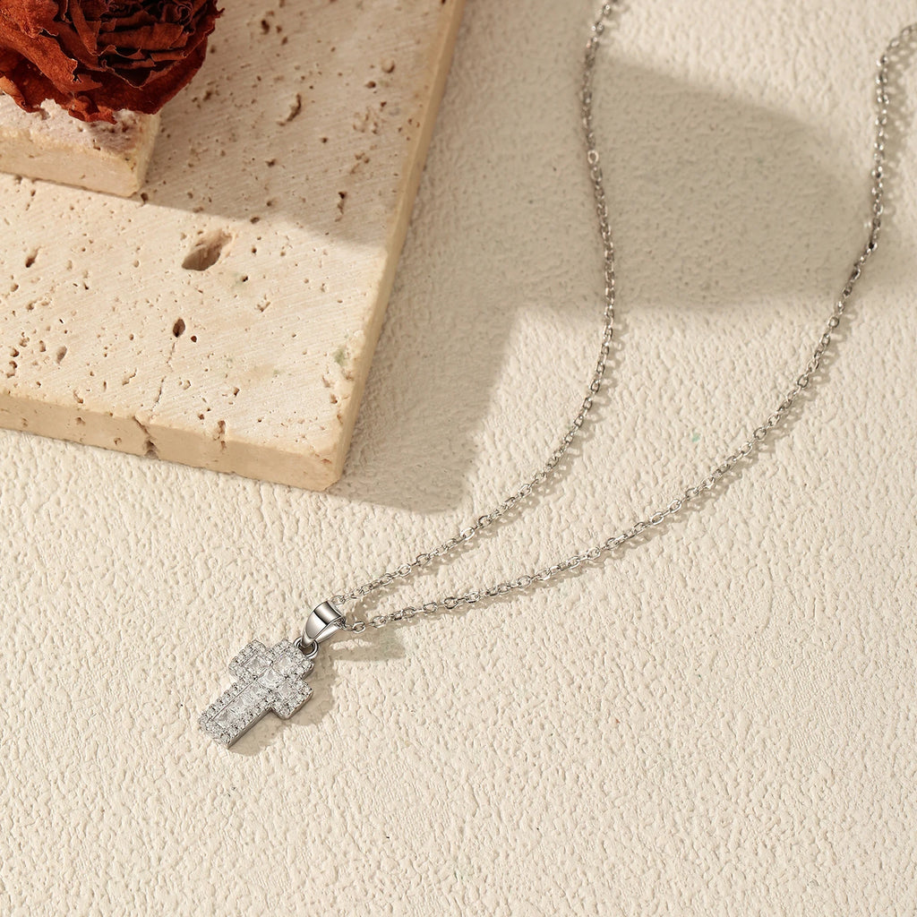 Silver-tone cross necklace arranged on a textured surface, showing the fine oval-link chain