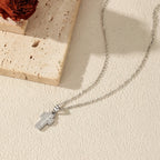 Silver-tone cross necklace arranged on a textured surface, showing the fine oval-link chain