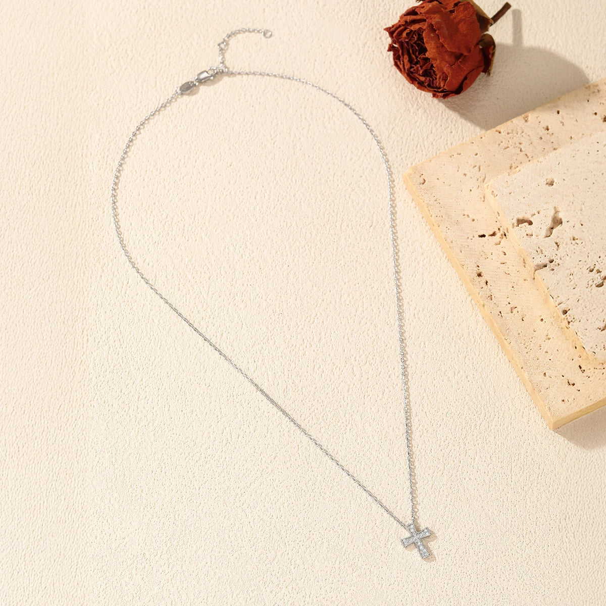 Silver-tone cross necklace flat lay showing the oval-link chain, clasp, and stone-filled pendant