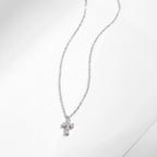 Fine oval-link chain and stone-set silver cross pendant arranged on a white surface