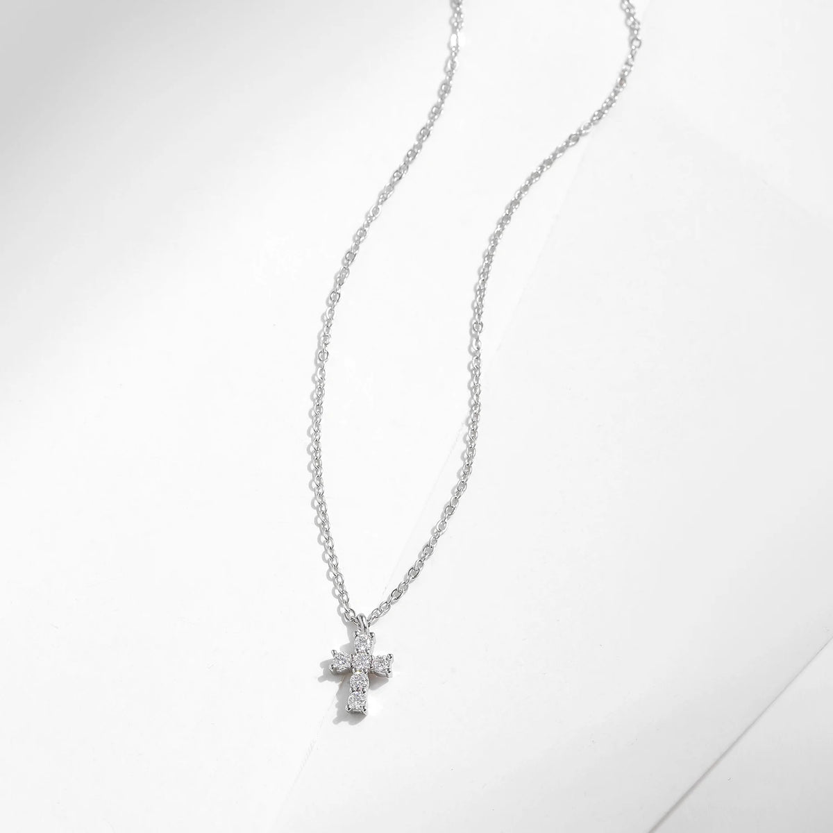 Fine oval-link chain and stone-set silver cross pendant arranged on a white surface