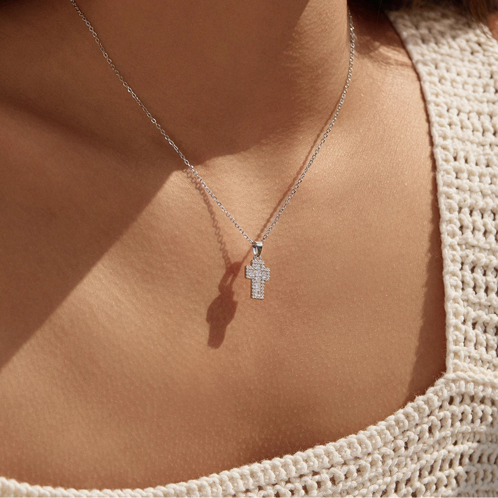 Small silver cross necklace worn at the collarbone with a sparkling stone-set cross pendant