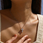 Stone-set cross pendant worn on a fine silver chain, shown against the chest in direct sunlight
