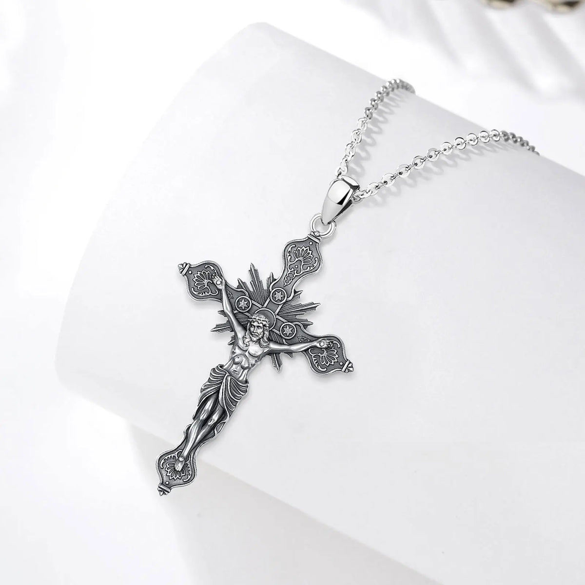 Sterling silver crucifix necklace displayed on a white curved surface with radiating rays and star circles
