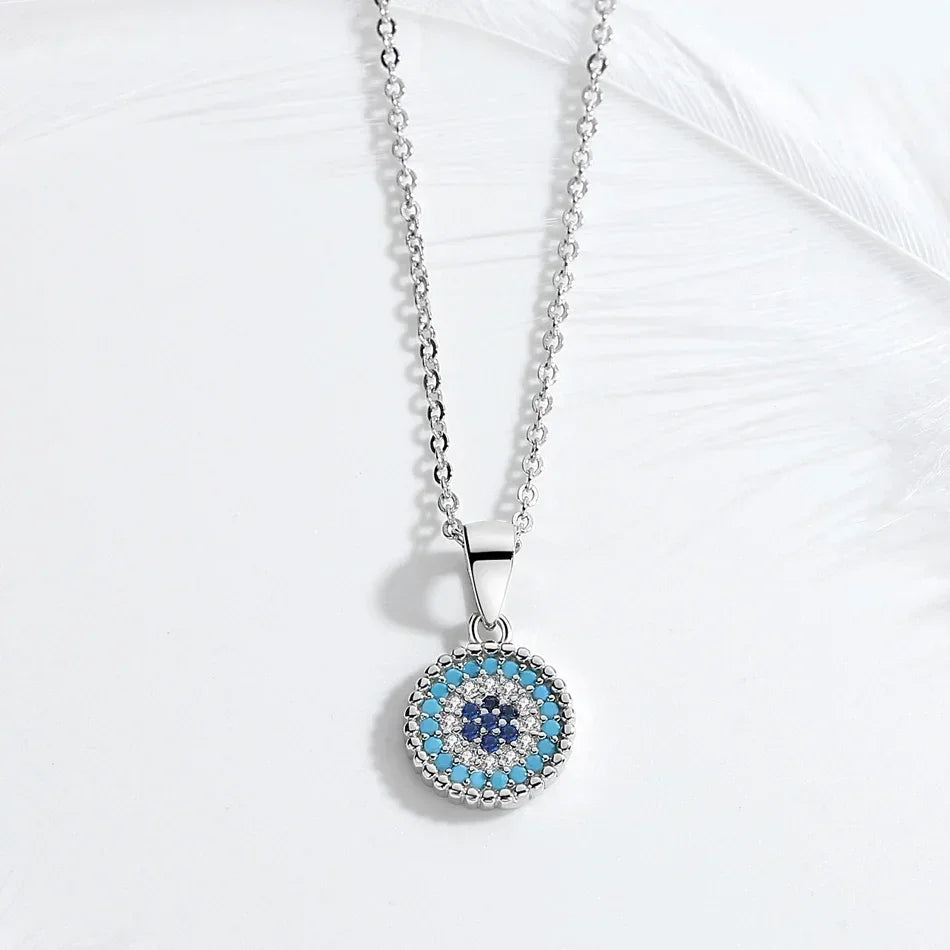 Silver-tone evil eye pendant necklace laid on a white surface with a feather in the background
