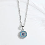 Silver-tone evil eye pendant necklace laid on a white surface with a feather in the background