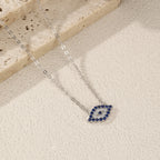 Silver evil eye necklace arranged on a textured light surface, showing the pointed blue stone outline