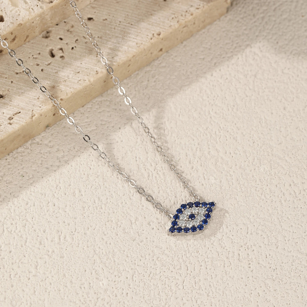 Silver evil eye necklace arranged on a textured light surface, showing the pointed blue stone outline