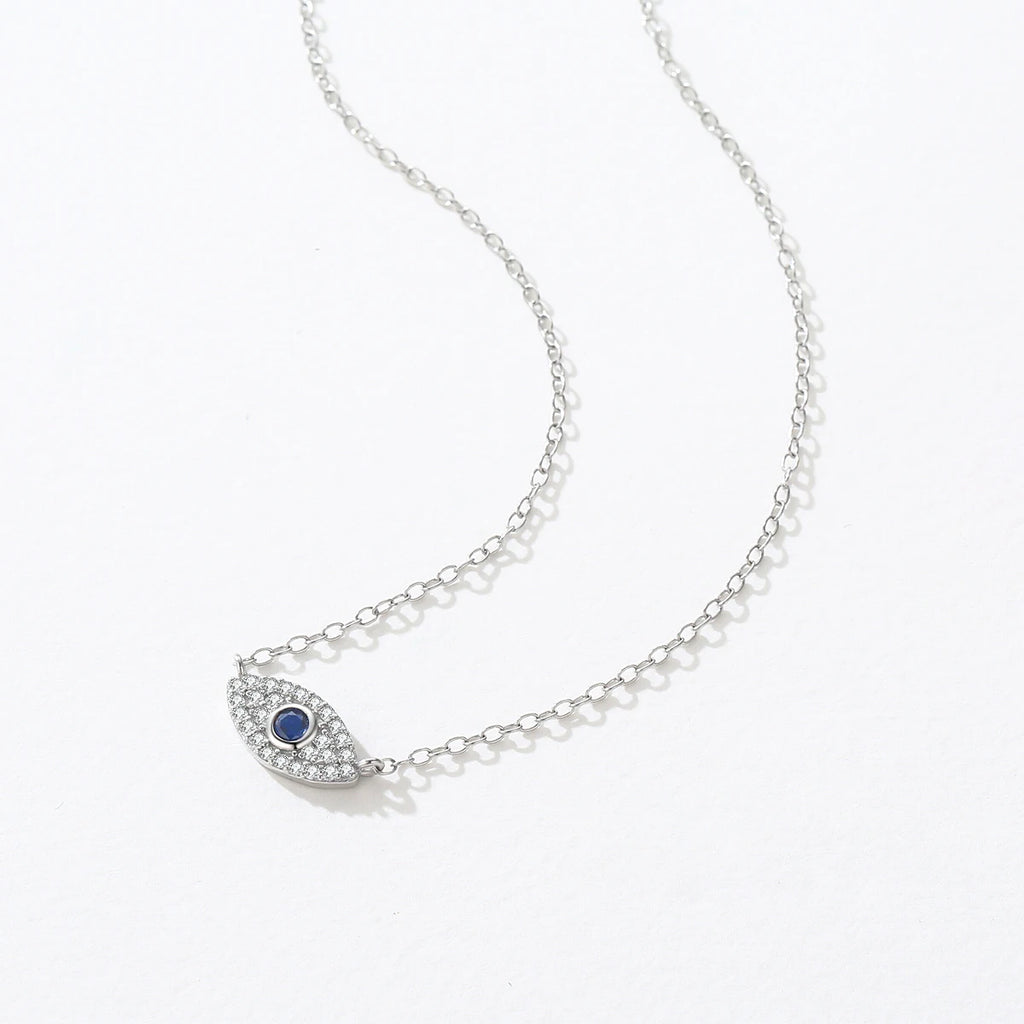 Silver-tone inline evil eye necklace laid on white with clear crystal outline and blue center stone