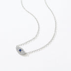 Silver-tone inline evil eye necklace laid on white with clear crystal outline and blue center stone