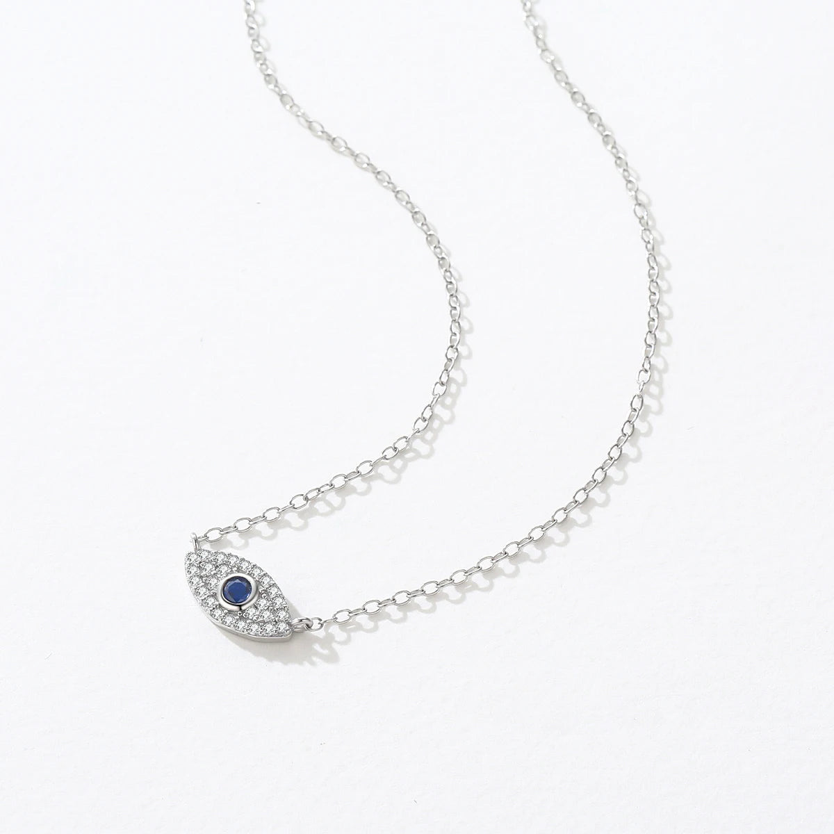 Silver-tone inline evil eye necklace laid on white with clear crystal outline and blue center stone