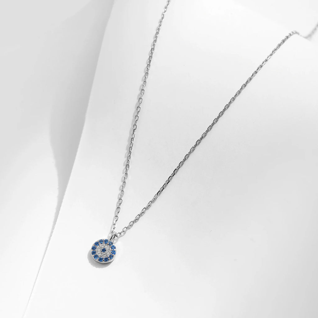 Silver-tone necklace with a round blue and clear stone evil eye pendant on a white display