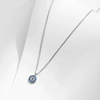 Silver-tone necklace with a round blue and clear stone evil eye pendant on a white display