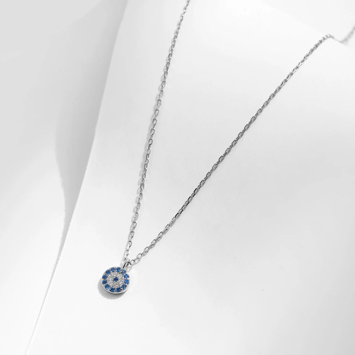 Silver-tone necklace with a round blue and clear stone evil eye pendant on a white display
