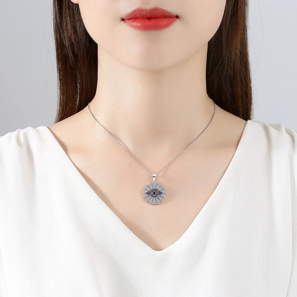 Silver-tone evil eye medallion necklace worn at the collarbone with a white V-neck top