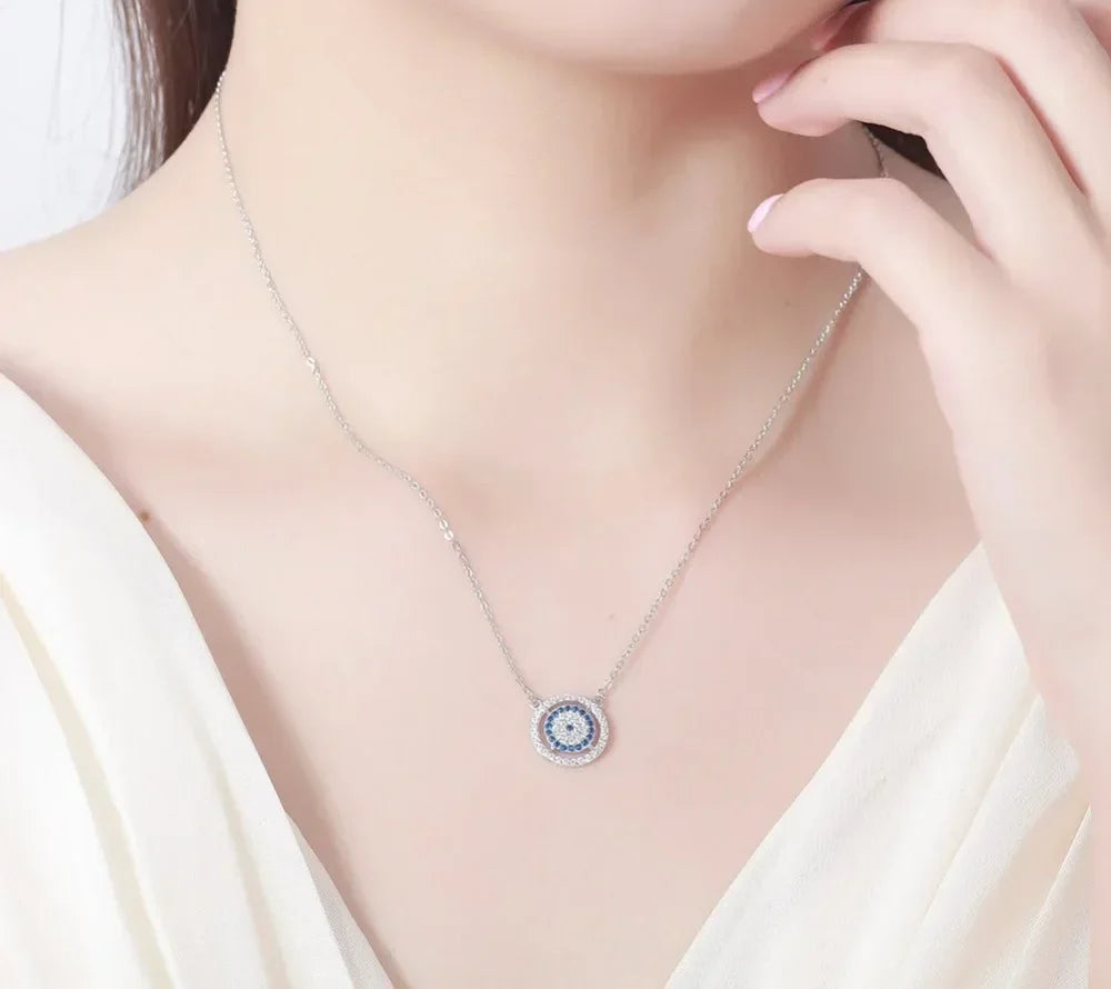 Silver-tone double halo evil eye necklace worn on the neck, showing the small blue and clear stone-set pendant