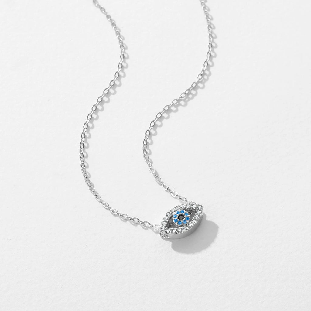 Silver-tone evil eye pendant on a white surface with clear outline stones and blue center stones