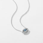 Silver-tone evil eye pendant on a white surface with clear outline stones and blue center stones