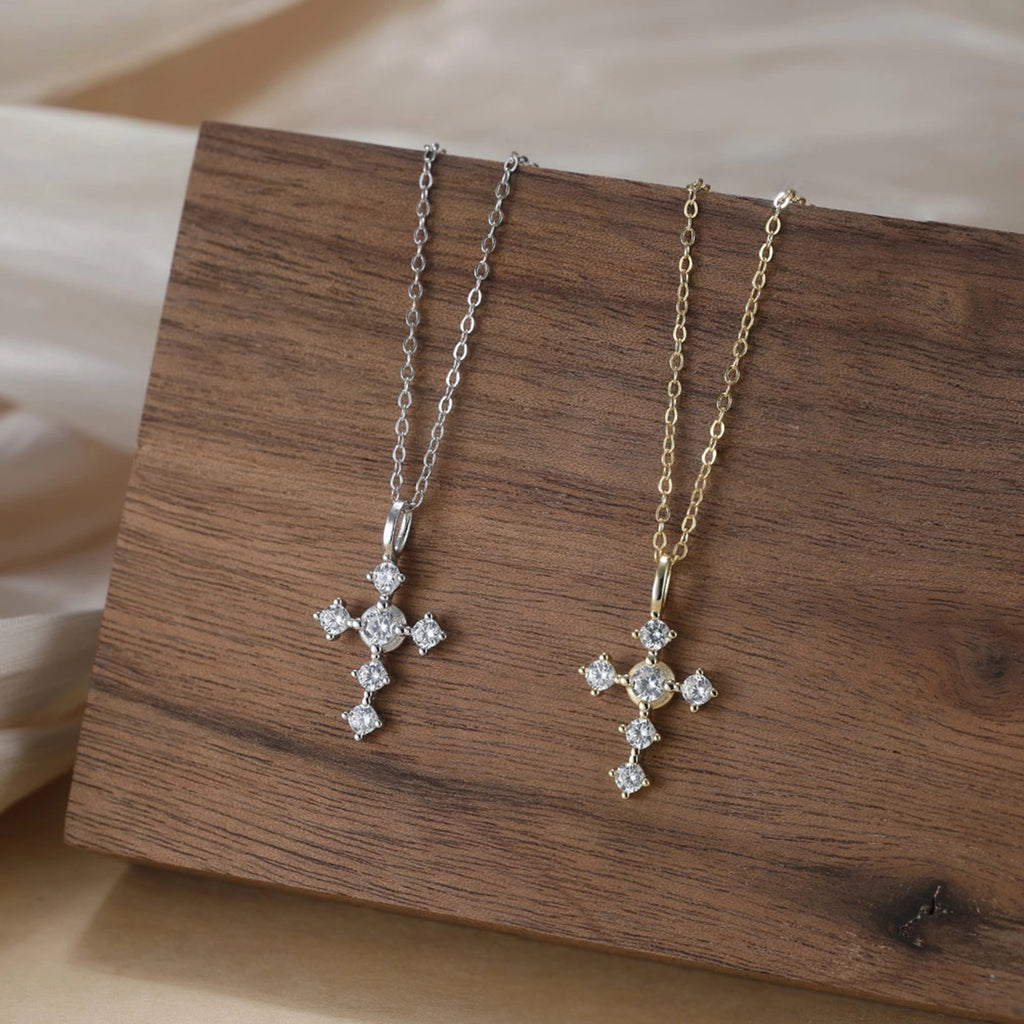 Sparkling silver cross necklaces with clear stones displayed on a wood block